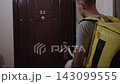 Food delivery courier with yellow thermal backpack giving order in plastic bag to happy man at apartment door, providing convenient service and customer satisfaction. 143099555
