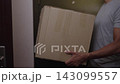 Closeup of courier hands over large cardboard package to recipient at apartment entrance. Concept of online shopping, shipping services and e-commerce, close-up, slow motion. 143099557