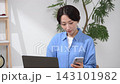 一名女子一邊操作電腦，一邊看著她的智慧型手機。 143101982