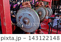 Close-up of a musician playing traditional Indonesian gongs suspended by ropes. The hands hold the mallet, striking the rustic metal instruments during a cultural performance with microphones set up. 143122148