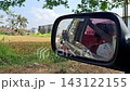 Video captured from inside moving vehicle focused on side mirror reflecting motorbikes trucks and scenic countryside scenery under bright sky. 143122155