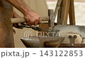 Close macro perspective focuses on impact of hammer face on workpiece, metal scale dust, and weathered texture of anvil top in outdoor forge. 143122853