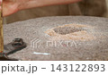 Closeup macro of the central feeding eye hopper of a rotating granite quern millstone filled with whole grain wheat while an artisan's hand grips the wooden handle to grind coarse wholemeal flour... 143122893