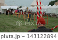 Medium shot captures red and white spiral-striped jousting lances held in foreground as medieval tournament arena prepares with mounted knights, squire, and white camp tents in background. 143122894