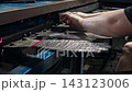 Worker rapidly positions knitted protective gloves on moving hand forms during industrial production. Manual handling keeps each glove aligned before next stage of factory processing. 143123006