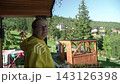woman yellow hoodie glasses drinking coffee chatting terrace mountain cottage, enjoying panoramic view mountains nature. background, wooden gazebo tall green trees. warm summer day. 143126398
