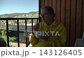 woman wearing yellow hoodie glasses having breakfast terrace country house overlooking mountains. enjoying nature eating slowly pleasure. background, mountain dotted numerous vacation cottages covered 143126405
