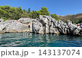 Limestone cliffs rise above calm coastal water, backed by dense green forest and mountain slopes. This Adriatic shoreline offers sheltered setting for coastal kayaking beneath blue sky 143137074