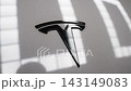 Tight close up of a black Tesla T emblem on white paint in an indoor showroom, shallow depth of field with subtle tilts and pans, reflections visible 143149083