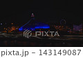 Aerial night view of the Latvian National Library in Riga during Staro 2025, terraces lit in blue, apex pink and white, neon mapping, Ferris wheel, river reflections. 143149087