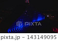 Aerial night view shows Latvian National Library in Riga lit vivid blue during Riga Staro 2025, with pink crown and projection mapping lines, red installs, and skyline. 143149095