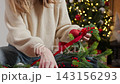 Woman Making DIY Christmas Garland with Red Ribbon and Ornament 143156293