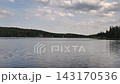 Wide view of still lake framed by dense evergreen trees, with small riverside house and distant dam towers on horizon, with lake, water, forest, evergreen detail, showing tree, shoreline, dam, tower 143170536
