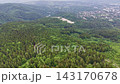 High altitude view showing dense green woodland across rolling hills, exposed sandy quarry near hilltop, and scattered suburban houses beyond, with soft overcast light and broad landscape context 143170678