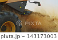 Combine harvester spreading straw and chaff across a field during harvest in slow motion with dust rising in the air 143173003