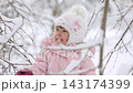 A child is having fun outdoors in winter forest. A little girl plays in a nature park against a snow covered trees background. Healthy lifestyle and winter holidays concept. 143174399