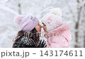 Mother and child are having fun outdoors in winter forest. A family plays in a nature park against a snow covered trees background. Healthy lifestyle and winter holidays concept. 143174611