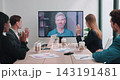Multiethnic business team waves to remote Caucasian boss on screen during office meeting. Multicultural colleagues greet manager warmly raising hands together 143191481