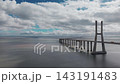 A wide drone shot reveals the bridge deck, repeated piers and open Tagus estuary near Lisbon, Portugal. 143191483