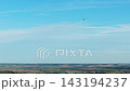 Distant hot air balloon flying high above farmland under clear blue sky. Small colorful aircraft over rural fields and low horizon. Scenic aerial flight with thin clouds and wide open sky above 143194237