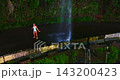 A female tourist enjoys nature while standing beneath a beautiful waterfall, with the spray splashing onto her 143200423