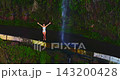 A female tourist enjoys nature while standing beneath a beautiful waterfall, with the spray splashing onto her 143200428