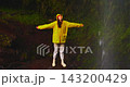 A female tourist enjoys nature while standing beneath a beautiful waterfall, with the spray splashing onto her 143200429