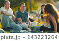 Friends gather at a park to enjoy food and drinks in a sunny afternoon setting 143223264