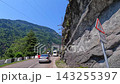 Vehicles pass roadworks, forward road view beside a rock wall on a narrow Georgian mountain route, illustrating traffic control, highway maintenance and transport safety in difficult terrain 143255397