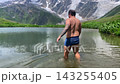 Male tourist bathing in rear view in alpine Namkuami Lake below Mount Shkhara near Ushguli, Svaneti, Georgia, travel scene for cold water recreation, trekking tourism, and mountain adventure promotion 143255405