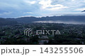 Aerial drone view overlooking Lake Batur and a cloud-wrapped mountain landscape at sunrise in Bali, Indonesia. Soft morning light reveals lakeside villages, cultivated fields and forested hills 143255506