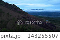 Aerial drone footage of colourful off-road jeeps crossing the dark volcanic slopes of Mount Batur at sunrise in Bali, Indonesia. Low clouds drift through the valley beyond the rugged mountain terrain 143255507