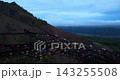 Aerial drone footage of off-road jeeps travelling across the volcanic slopes of Mount Batur at sunrise in Bali, Indonesia. The elevated view shows rugged black terrain and winding tracks 143255508