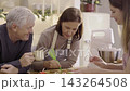 Group of people decorating festive gingerbread biscuits with colorful cream icing piping bags around wooden table during Christmas. Happy caucasian family enjoy baking and decorating gingerbread. 143264508