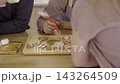 Group of people decorating festive gingerbread biscuits with colorful cream icing piping bags around wooden table during Christmas. Happy caucasian family enjoy baking and decorating gingerbread. 143264509