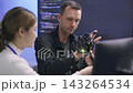 Software developers analyzing robotic prosthetic hand hardware while discussing code algorithm in high tech research office. Collaborating on artificial intelligence technology in laboratory. 143264534