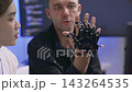Software developers analyzing robotic prosthetic hand hardware while discussing code algorithm in high tech research office. Collaborating on artificial intelligence technology in laboratory. 143264535