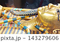 Tutankhamun's golden burial mask featuring blue inlays, a headdress, and arms crossed over the chest holding a crook and flail 143279606