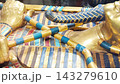 Tutankhamun's golden burial mask featuring blue inlays, a headdress, and arms crossed over the chest holding a crook and flail 143279610