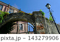 Old Stone Arch with Metal Gate and Green Ivy Among Weathered Historic Buildings in Kamianets Podilskyi Ukraine 143279906