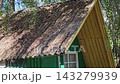 Small green wooden cabin with old roof surrounded by tall pine trees in peaceful summer forest near river 143279939