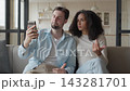 Stylish Couple Talking On Smartphone Video Call While Sitting On Sofa 143281701