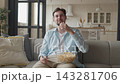 Man Eating Popcorn And Watching TV While Sitting On Sofa At Home 143281706