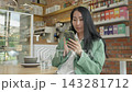 Modern Woman Scrolling And Swiping Smartphone Screen In Cozy Urban Cafe 143281712