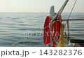 A red life jacket and a coil of rope on the railing of a yacht sailing in the open sea 143282376