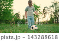 Little boy plays soccer on green grass. Kid plays football, city park. Child kicks soccer ball outdoors summer. Happy family. Athletic child leads active lifestyle. Kid boy footballer city park, sport 143288618