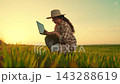 Female farmer with laptop tends green crop shoots in field, assessing future harvest. Woman farmer works computer in green field. Agronomist works in rural setting. Agricultural business. countryside 143288619