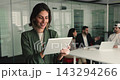 Smiling Mexican businesswoman standing in meeting room using tablet device 143294266