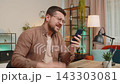 Upset displeased young businessman using smartphone reading bad news sitting at table in living room 143303081