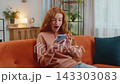 Happy young woman using cellphone celebrating success victory winning lottery on sofa in living room 143303083